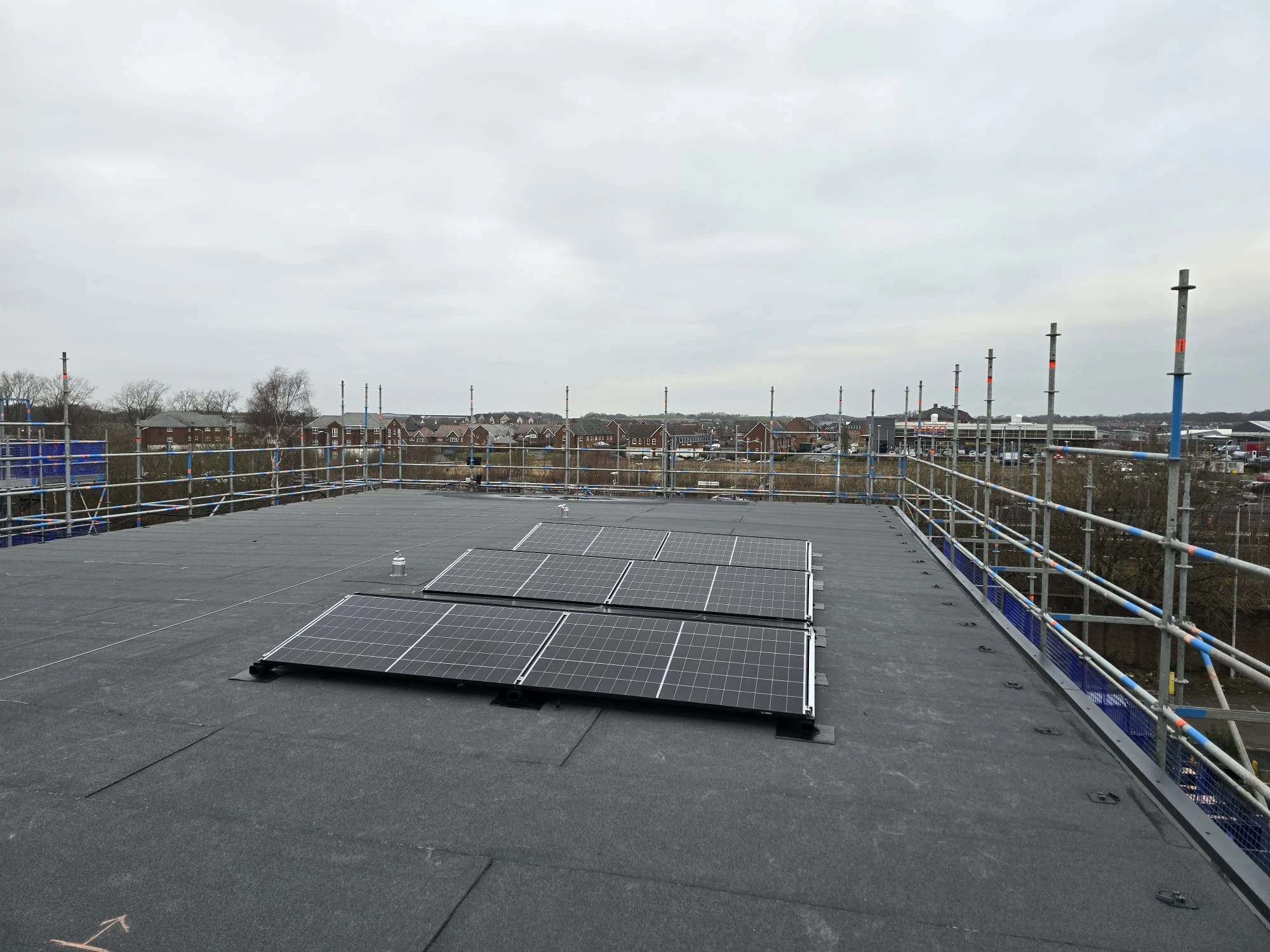 Rooftop with solar panels, surrounded by scaffolding, overlooking a cloudy sky and distant buildings.
